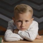 boy in white long sleeve shirt resting head on wooden table
