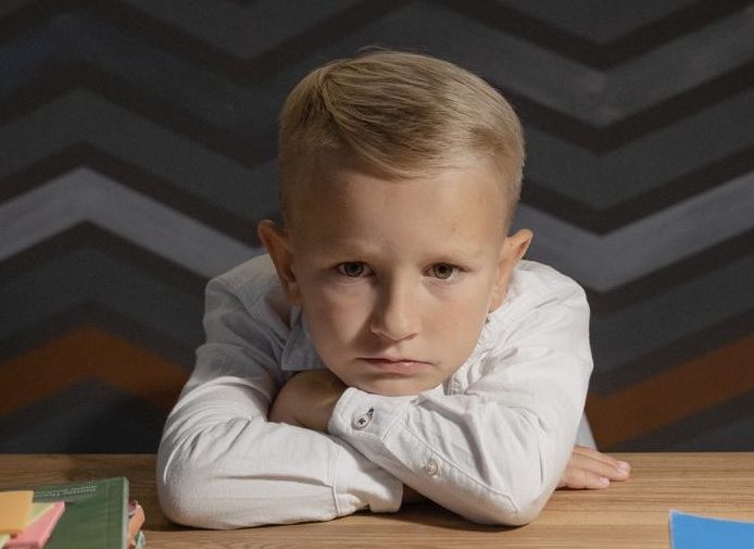 boy in white long sleeve shirt resting head on wooden table